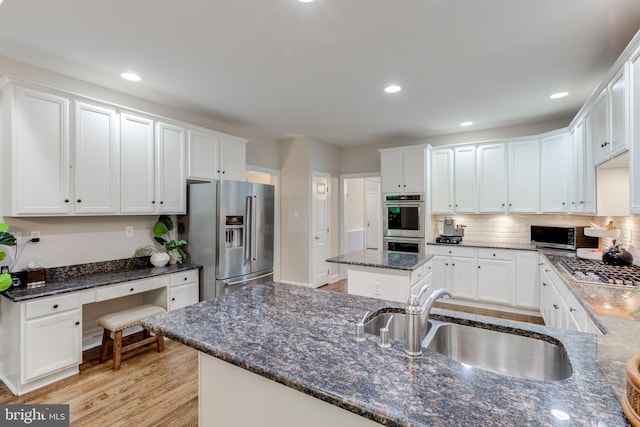 kitchen with appliances with stainless steel finishes, a sink, white cabinets, dark stone countertops, and recessed lighting