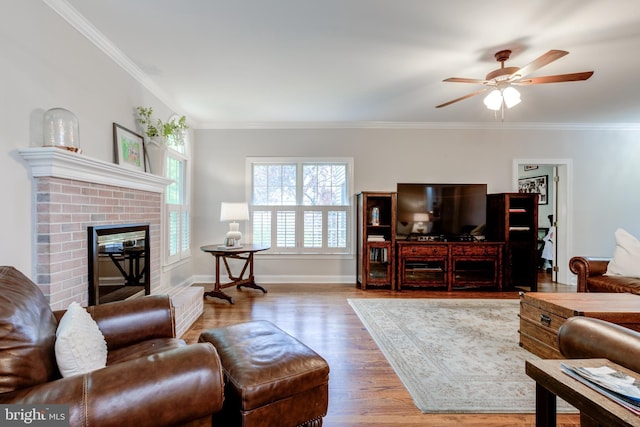 living room with wood finished floors, crown molding, ceiling fan, a fireplace, and baseboards