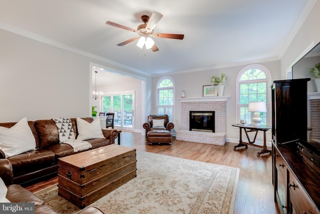 living area with a brick fireplace, plenty of natural light, a ceiling fan, crown molding, and wood finished floors