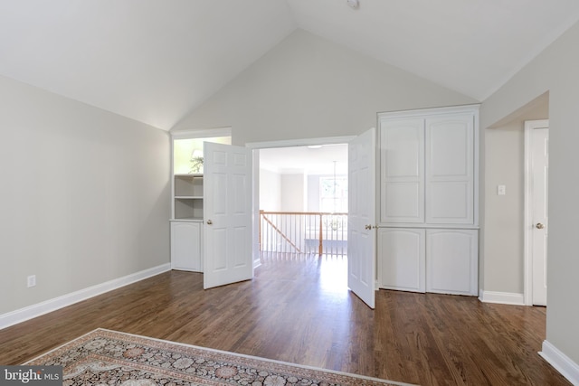 empty room with wood finished floors, high vaulted ceiling, and baseboards