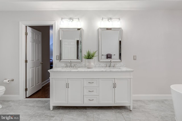 bathroom featuring toilet, double vanity, baseboards, and a freestanding tub