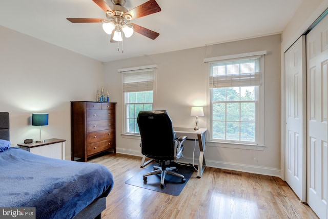 bedroom with light wood-type flooring, baseboards, a ceiling fan, an office area, and a closet