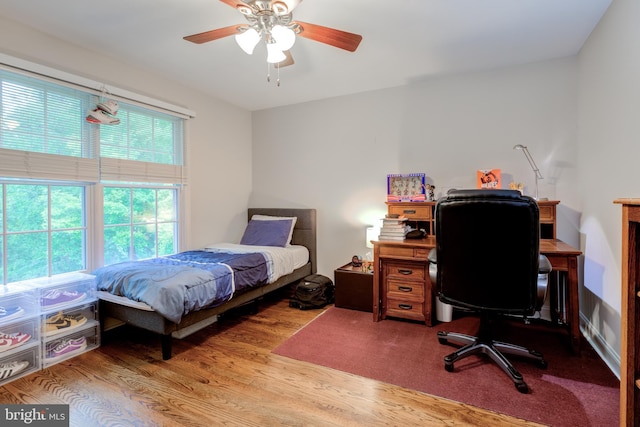 bedroom with wood finished floors, an office area, and a ceiling fan