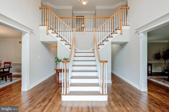 stairway with wood finished floors, baseboards, ornamental molding, and a high ceiling