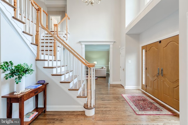 entryway featuring wood finished floors, a towering ceiling, stairway, baseboards, and a chandelier