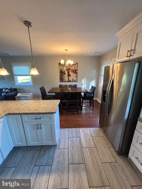 kitchen featuring stainless steel fridge, wood tiled floors, white cabinets, light stone countertops, and decorative light fixtures