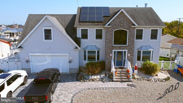 view of front facade featuring a gate, roof mounted solar panels, fence, and a garage
