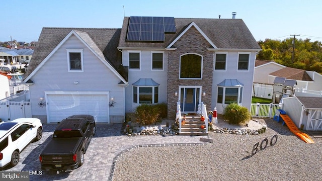 view of front of property featuring a gate, roof mounted solar panels, fence, an attached garage, and driveway