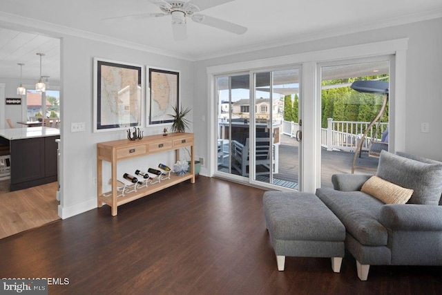 living area with ornamental molding, ceiling fan, wood finished floors, and baseboards