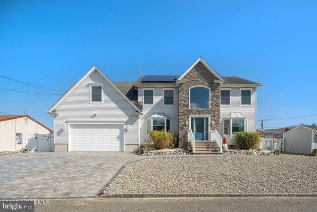 traditional-style home featuring solar panels, decorative driveway, a garage, fence, and a gate