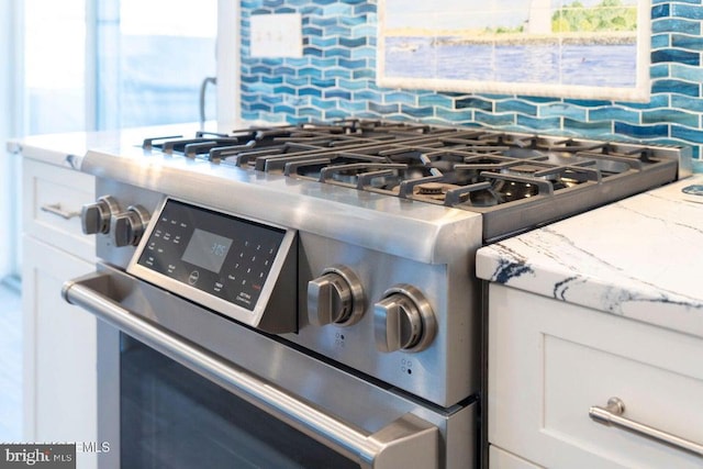 kitchen view of stainless steel gas stove, light stone counters, backsplash, and white cabinets