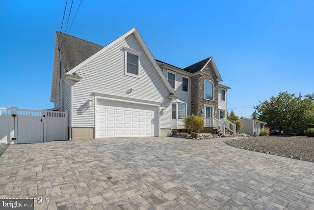 view of front facade featuring an attached garage, fence, a shed, a gate, and decorative driveway