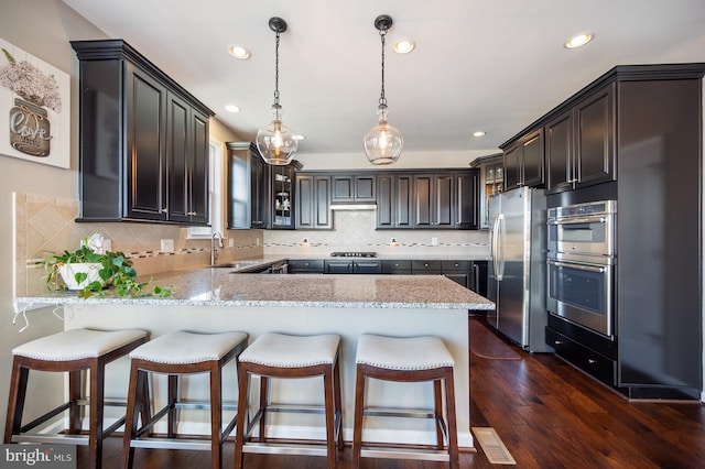 kitchen featuring appliances with stainless steel finishes, a sink, a peninsula, glass insert cabinets, and light stone countertops
