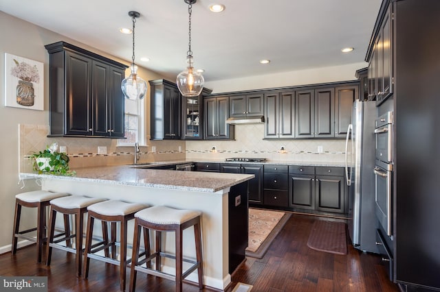kitchen with a peninsula, appliances with stainless steel finishes, a kitchen breakfast bar, dark wood-type flooring, and tasteful backsplash