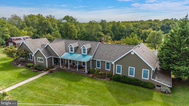 view of front of house featuring a front yard, covered porch, a chimney, a wooded view, and a standing seam roof
