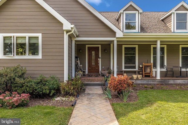 entrance to property featuring covered porch, a lawn, and a shingled roof
