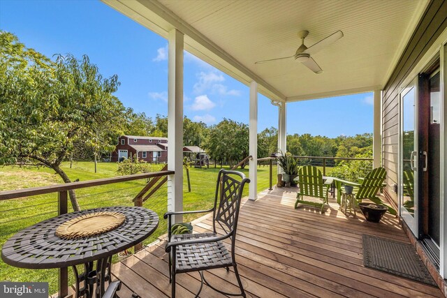 wooden terrace with ceiling fan, a lawn, view of wooded area, and a porch