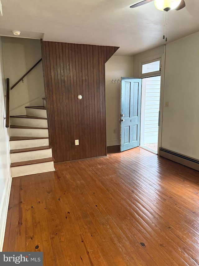 unfurnished living room featuring hardwood / wood-style floors, stairway, ceiling fan, and baseboards