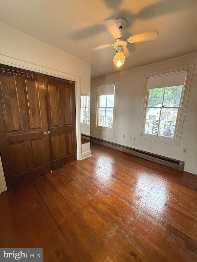 unfurnished bedroom with hardwood / wood-style flooring, a closet, baseboard heating, baseboards, and a ceiling fan