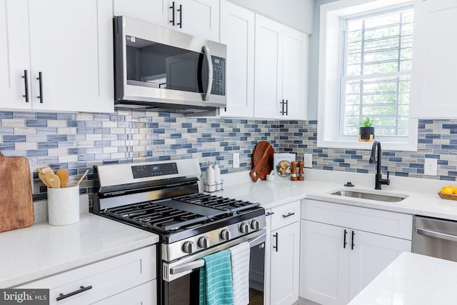 kitchen with stainless steel appliances, a sink, white cabinets, backsplash, and light stone countertops