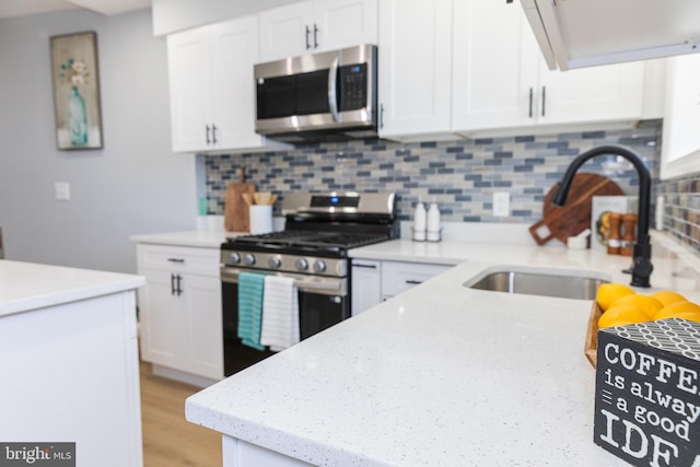 kitchen with appliances with stainless steel finishes, a sink, white cabinets, and backsplash