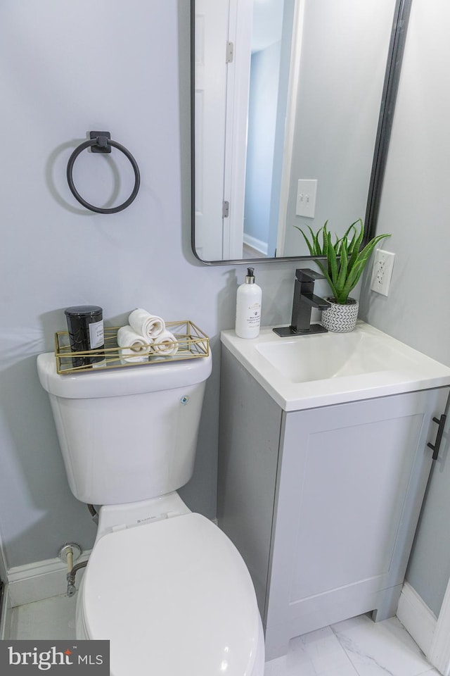 bathroom with toilet, vanity, marble finish floors, and baseboards