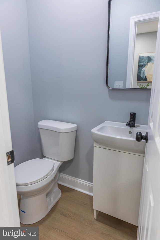 bathroom with toilet, vanity, wood finished floors, and baseboards