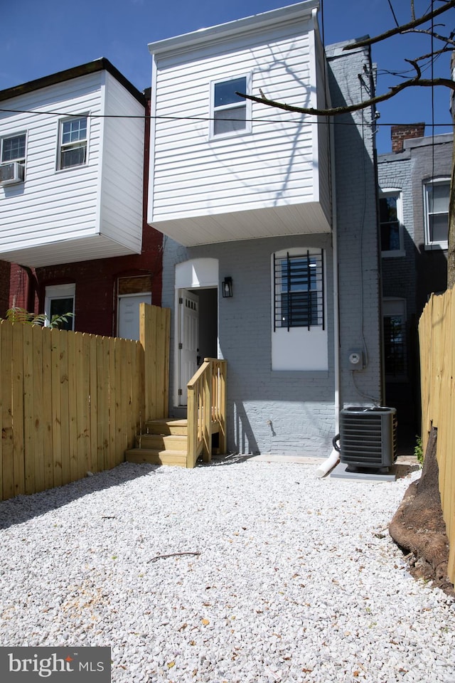 view of front of house featuring brick siding, cooling unit, and fence