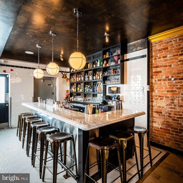 community bar area featuring brick wall, hardwood / wood-style flooring, and hanging light fixtures