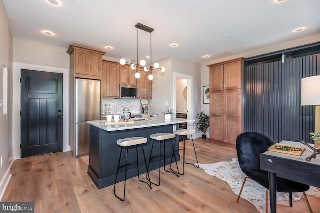 kitchen with appliances with stainless steel finishes, light wood finished floors, a kitchen bar, tasteful backsplash, and light countertops