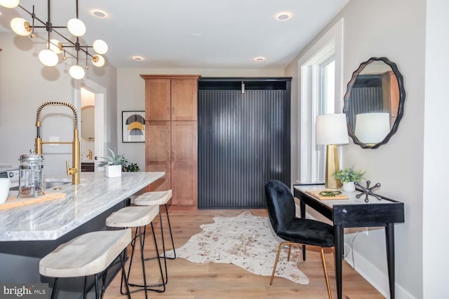 kitchen featuring light wood-type flooring, brown cabinetry, a kitchen breakfast bar, light stone counters, and pendant lighting