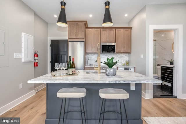 kitchen with stainless steel appliances, a kitchen bar, baseboards, light wood-style flooring, and recessed lighting