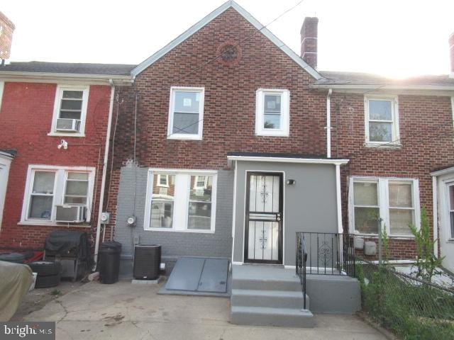 view of front of home featuring a chimney, central air condition unit, brick siding, and a patio area