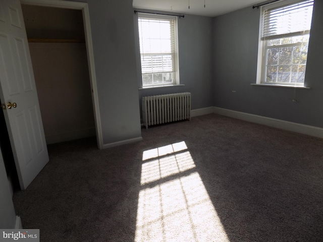 unfurnished bedroom with radiator, multiple windows, carpet floors, and baseboards