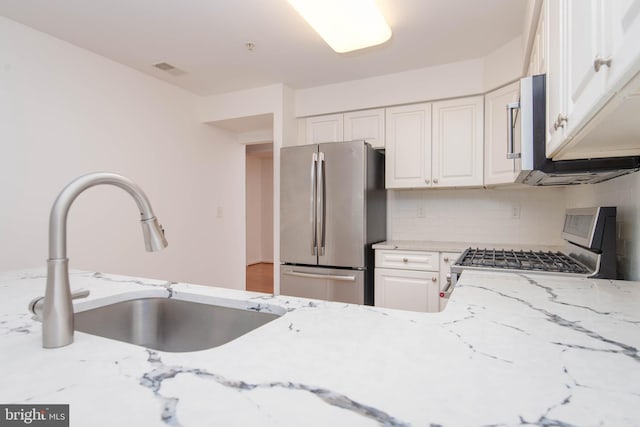 kitchen featuring appliances with stainless steel finishes, a sink, white cabinetry, and light stone counters