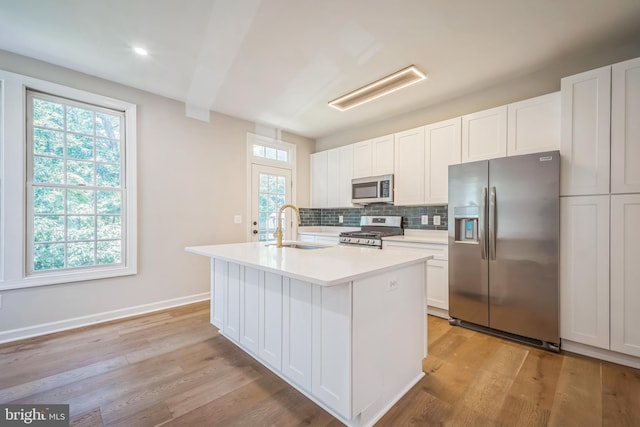 5561 Jowett Ct, Alexandria, VA 22315 - kitchen featuring appliances with stainless steel finishes, light countertops, decorative backsplash, a kitchen island with sink, and plenty of natural light