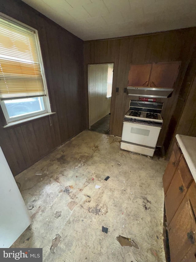 kitchen with white gas stove and wood walls