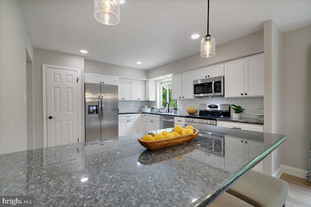 kitchen featuring stainless steel appliances, tasteful backsplash, white cabinetry, pendant lighting, and baseboards