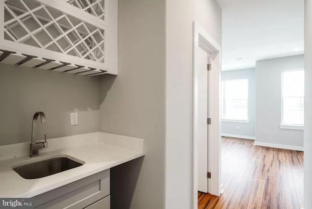 bar with a sink, light wood-style flooring, and baseboards