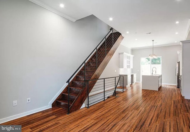 unfurnished living room featuring dark wood finished floors, crown molding, baseboards, a chandelier, and a sink