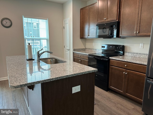 kitchen with black appliances, a sink, wood finished floors, and a center island with sink