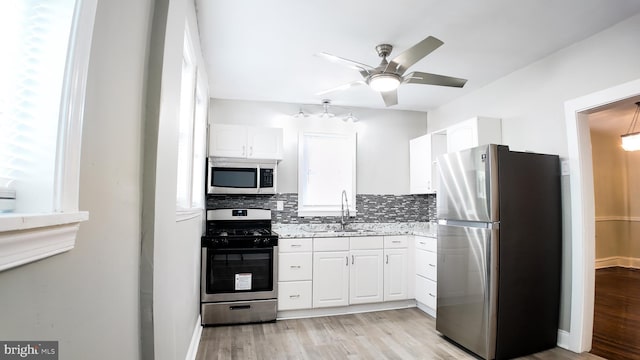 kitchen featuring appliances with stainless steel finishes, a sink, decorative backsplash, white cabinetry, and light wood finished floors