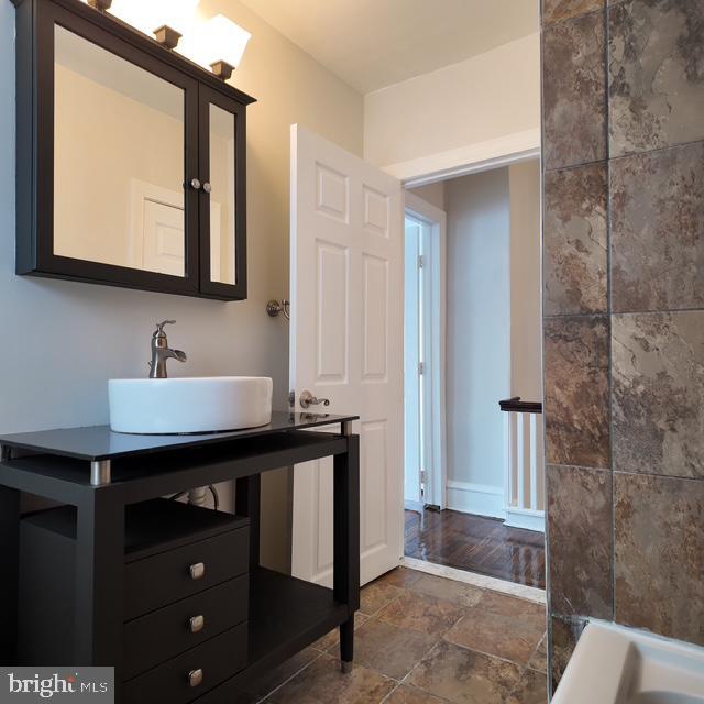 bathroom with stone finish floors, a sink, and baseboards