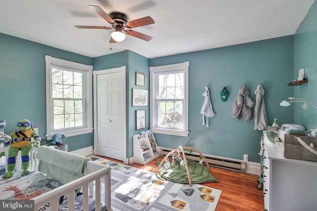 bedroom with baseboard heating, multiple windows, a closet, and wood finished floors