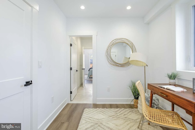 corridor featuring light wood finished floors, a desk, baseboards, and recessed lighting
