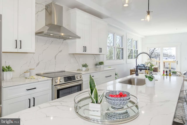 kitchen featuring stainless steel range with electric cooktop, wall chimney exhaust hood, white cabinets, a sink, and decorative backsplash
