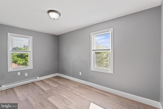 spare room featuring baseboard heating, light wood-type flooring, and baseboards