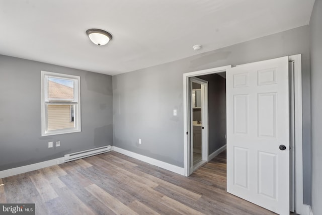 spare room featuring a baseboard heating unit, baseboards, wood finished floors, and a smoke detector