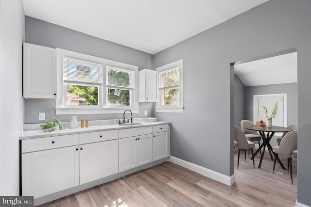 kitchen with a sink, white cabinetry, light wood finished floors, light countertops, and baseboards