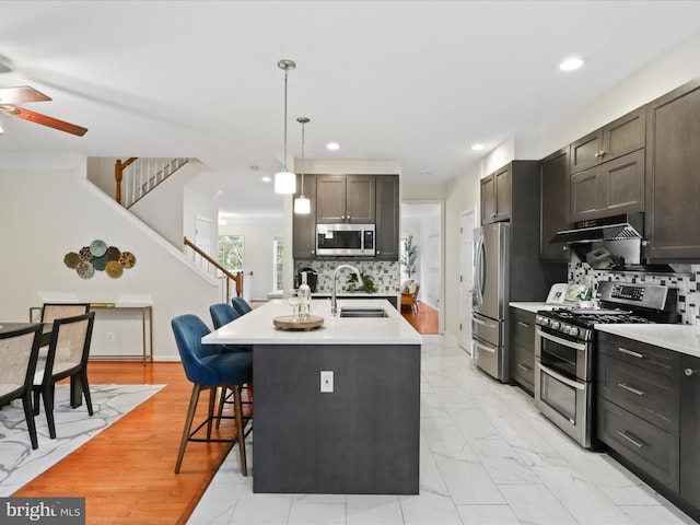 kitchen featuring appliances with stainless steel finishes, a sink, ceiling fan, under cabinet range hood, and light countertops